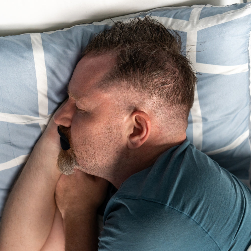 Mann sover på siden med soveteip for å redusere snorking og forbedre søvn.
