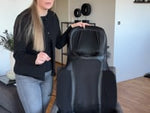 Zenova massasjestol i svart design, plassert på en stol i en moderne stue. Perfekt for avslappende massasje hjemme.